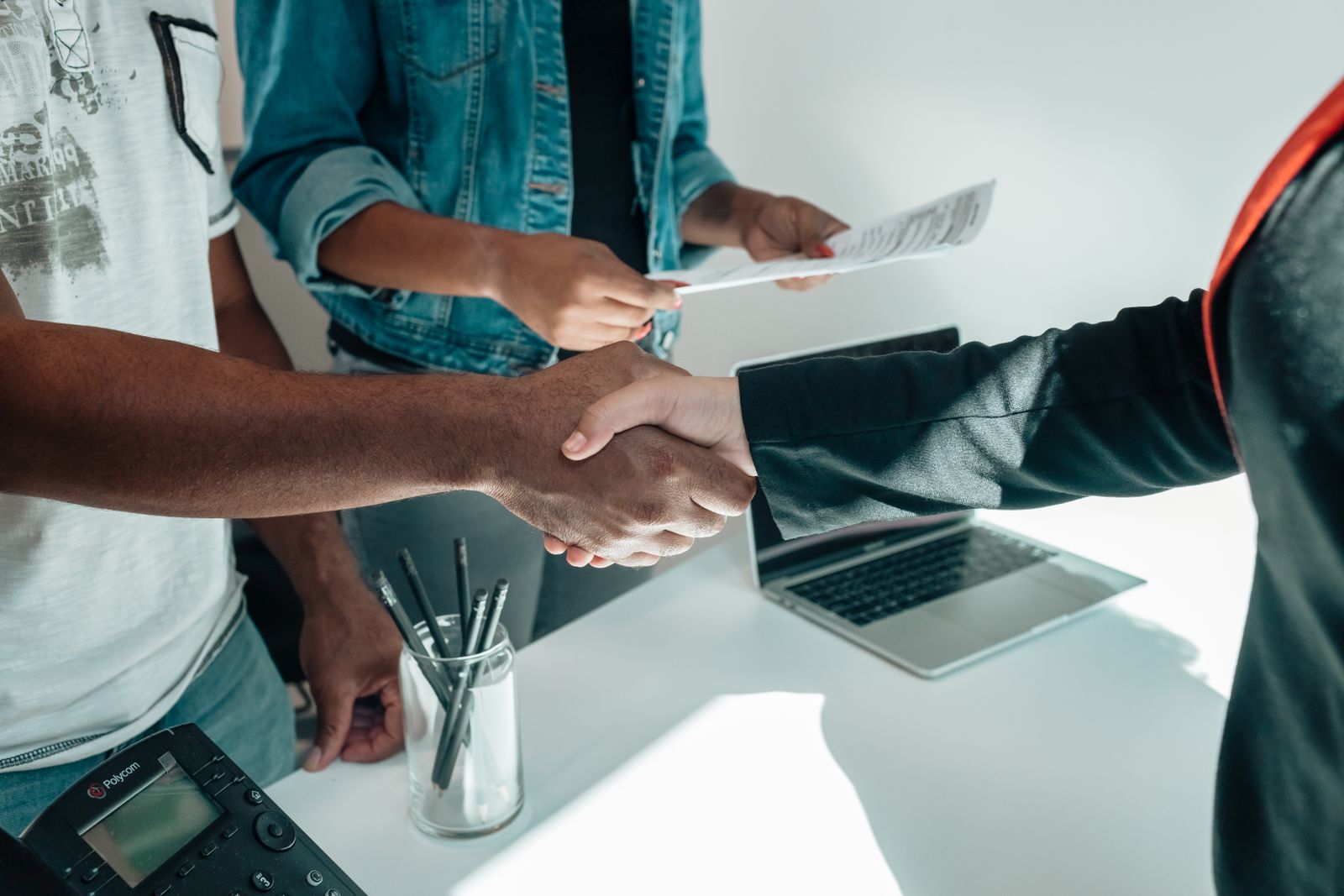 Händedruck über einem Schreibtisch mit Laptop und Unterlagen